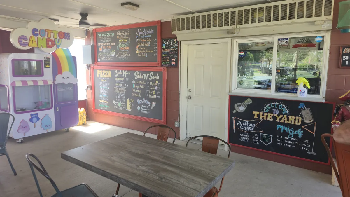 Chalkboard menus, the cotton candy machine, and mini golf and batting cage pricing inside The Yard's concession area